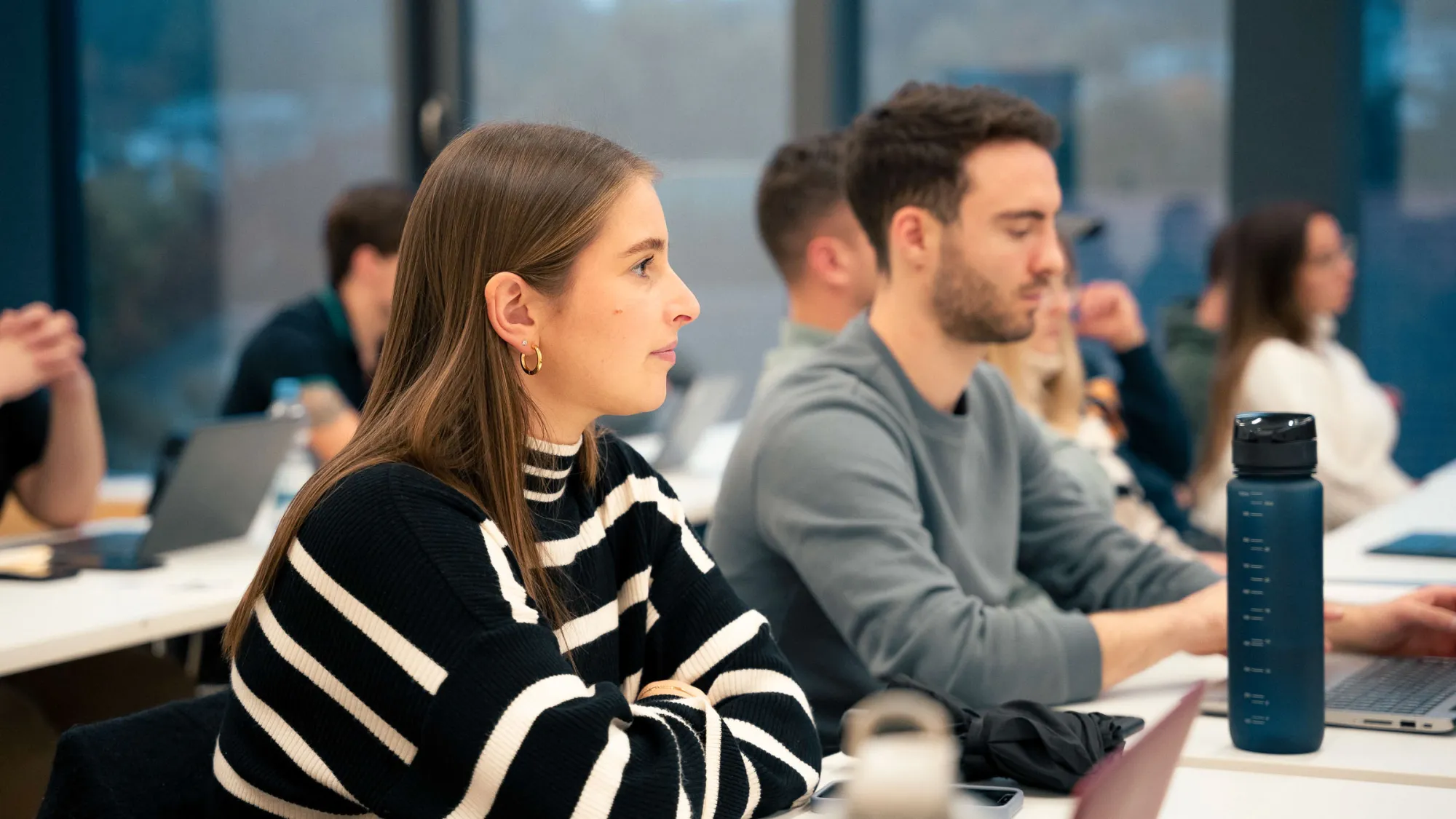 Nahaufnahme einer Studierenden von der Seite, im Hintergrund weitere Studierende unscharf. 