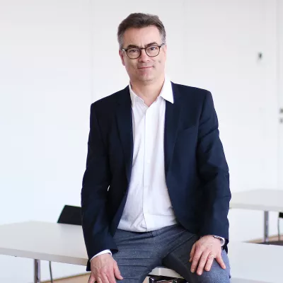 Professor Klemens Ehret sitzt im Vorlesungsraum und schaut in die Kamera