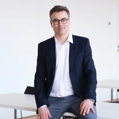 Professor Klemens Ehret sitzt im Vorlesungsraum und schaut in die Kamera