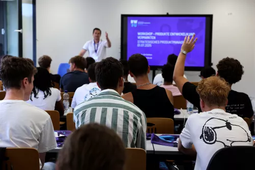 RWU zu Gast im RNG Wangen. Schüler:innen sitzen in einem Seminarraum. Im Hintergrund steht ein Dozent der RWU, ein Schüler meldet sich.