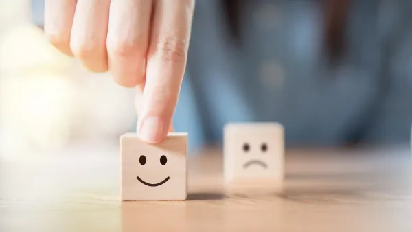 Hand wählt lächelnden Smiley aus, der auf einen kleinen Holzwürfel aufgedruckt ist.