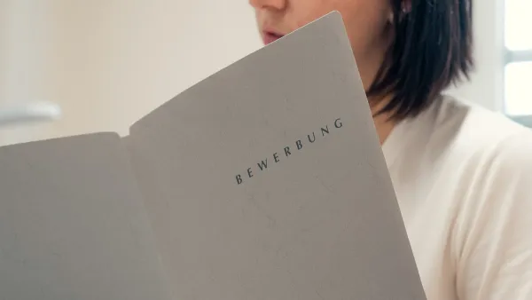 Halbnahe Aufnahme einer Person an einem Schreibtisch mit einer Bewerbungsmappe in der Hand. 