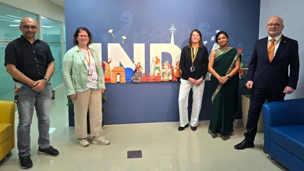 Delegation der RWU besucht Indien und steht gemeinsam mit Gastgebern des Unternehmens ifm vor einer dekorativen Wand.