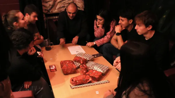 Studierende sitzen um einen Tisch mit Geschenken und spielen Schrottwichteln.