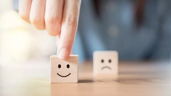 Hand wählt lächelnden Smiley aus, der auf einen kleinen Holzwürfel aufgedruckt ist.