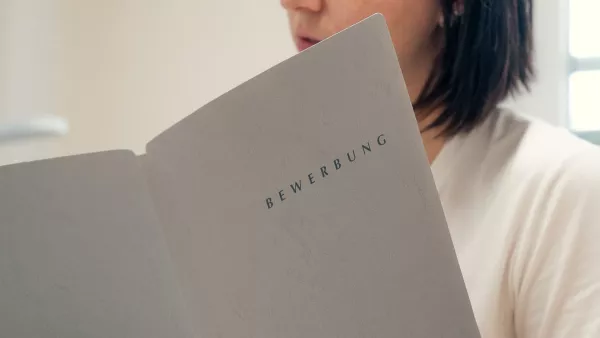 Halbnahe Aufnahme einer Person an einem Schreibtisch mit einer Bewerbungsmappe in der Hand.