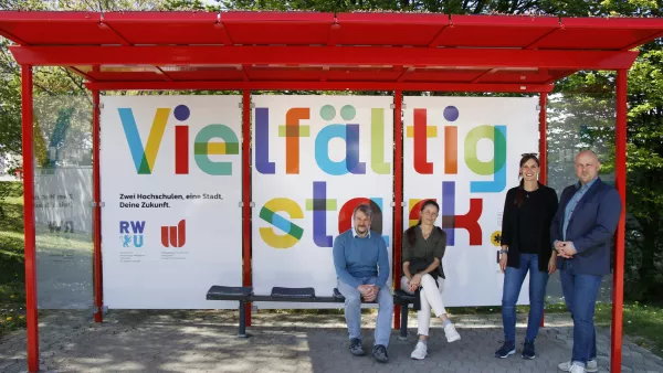 Vertreter*innen der Stadt, der PH und der RWU in der neu gestalteten Bushaltestelle. An der Rückwand der Slogan "Vielfältig stark."