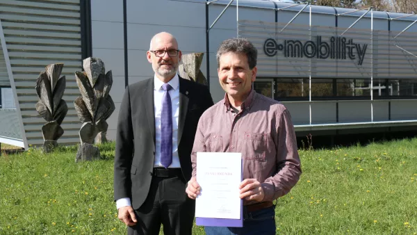 Prof. Andreas Siggelkow und der RWU Rektor, Prof. Thomas Spägele, stehen vor dem E-Mobility-Labor der RWU.