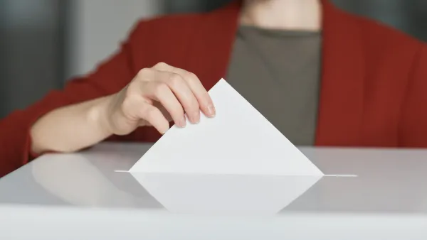 Frau mit Mundschutz wirft Zettel in Wahlurne.