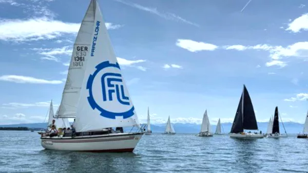 Das Segelboot des RWU-Segelclubs auf dem Bodensee, im Hintergrund sind viele weitere Boote und die Berge zu sehen.