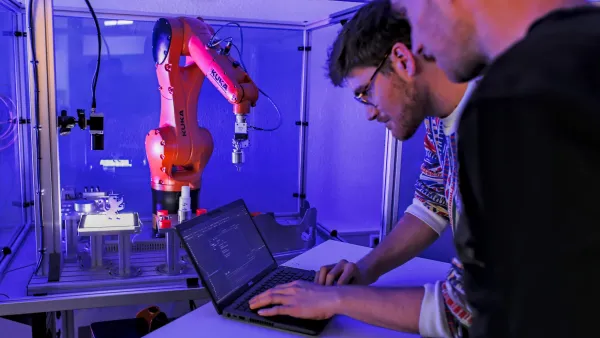 Studenten im Labor programmieren einen KUKA-Roboterarm.
