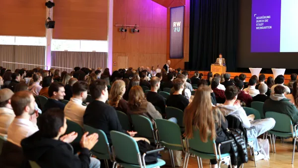 Eine große Gruppe an Erstsemesterstudierenden schaut in Richtung einer Bühne auf der Oberbürgermeister Clemens Moll spricht.entrum Weingarten.