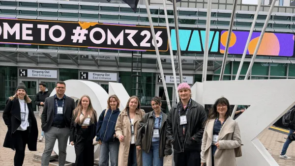 Eine Gruppe von Studierenden der RWU posiert vor dem Eingangsbereich der OMR 2026 in Hamburg. Im Hintergrund ist ein großes digitales Banner mit dem Schriftzug „WELCOME TO #OMR26“ sowie mehrere schwarze OMR-Flaggen zu sehen. Die Gruppe steht lächelnd vor einer großen weißen Skulptur auf dem Vorplatz der Messehallen.