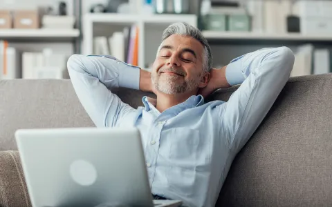 Mann sitzt am Laptop und lehnt sich entspannt zurück